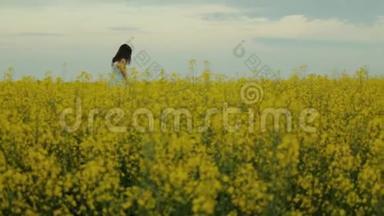 美丽的女孩走在黄花的田野里。 微笑和欢笑